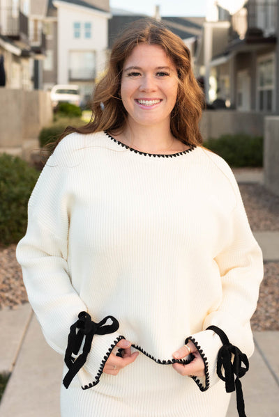 Front view of the plus size cream knit sweater with black trim and black bows on the wrist