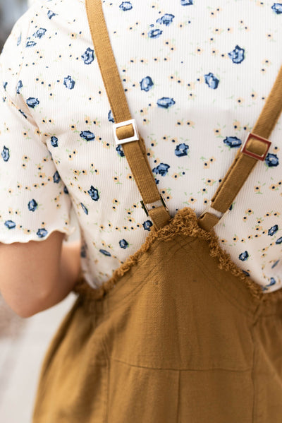 Back view of the dark mustard washed jumpsuit with adjustable straps and frayed edges