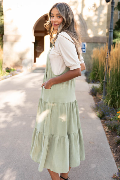 Side view of the sage green overall dress with pockets