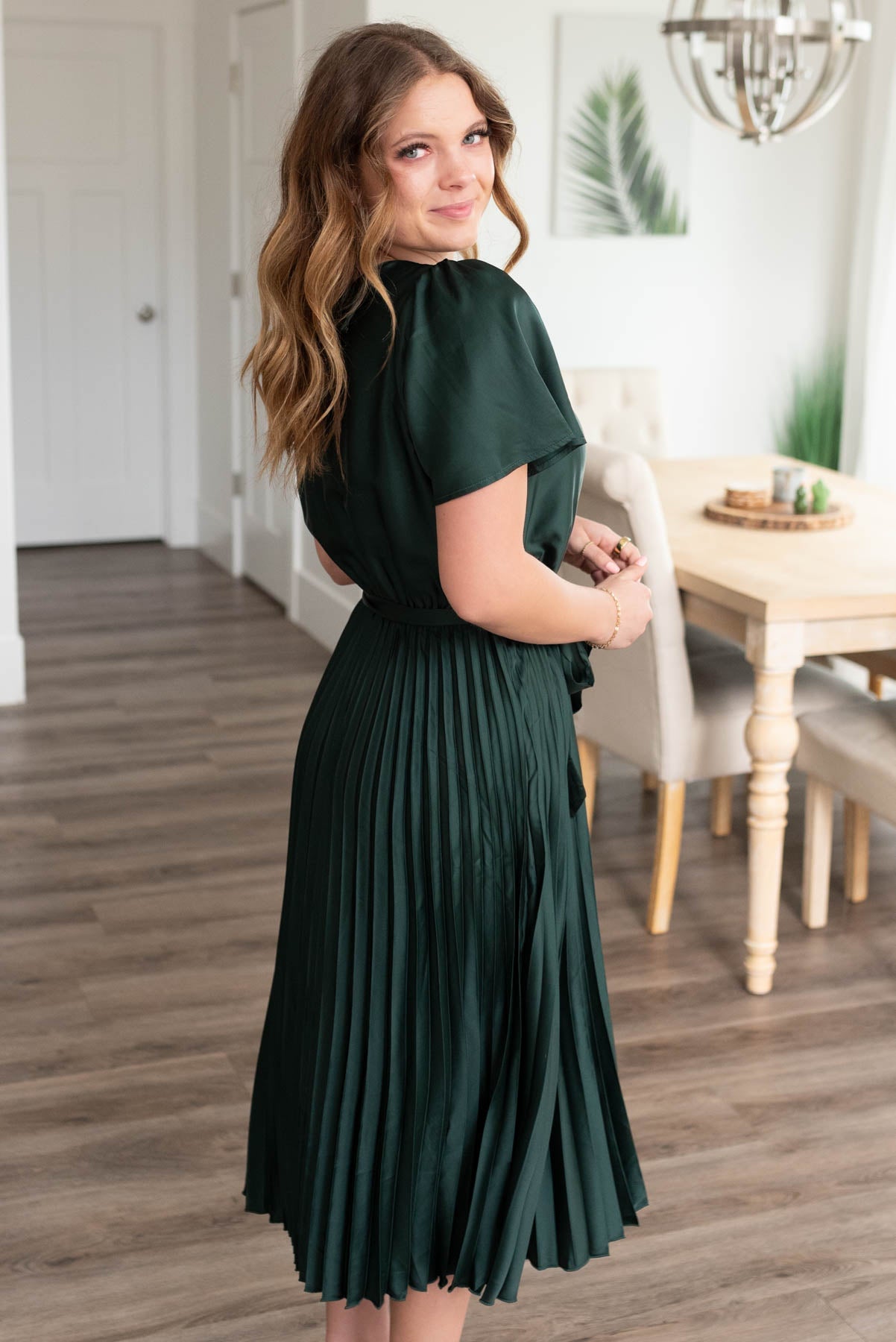 Side view of the junter green satin pleat dress with a tie at the waist