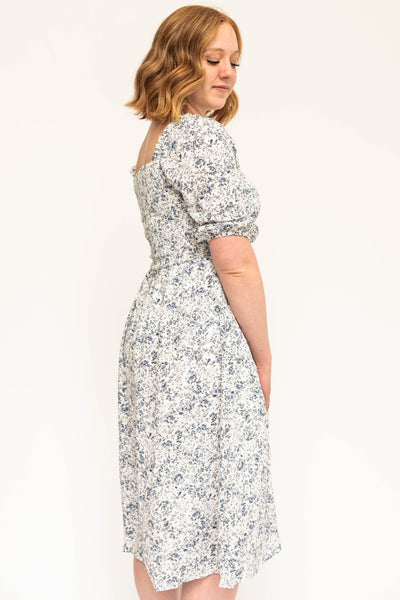 Side view of a blue and white short sleeve floral dress with a smocked bodice.