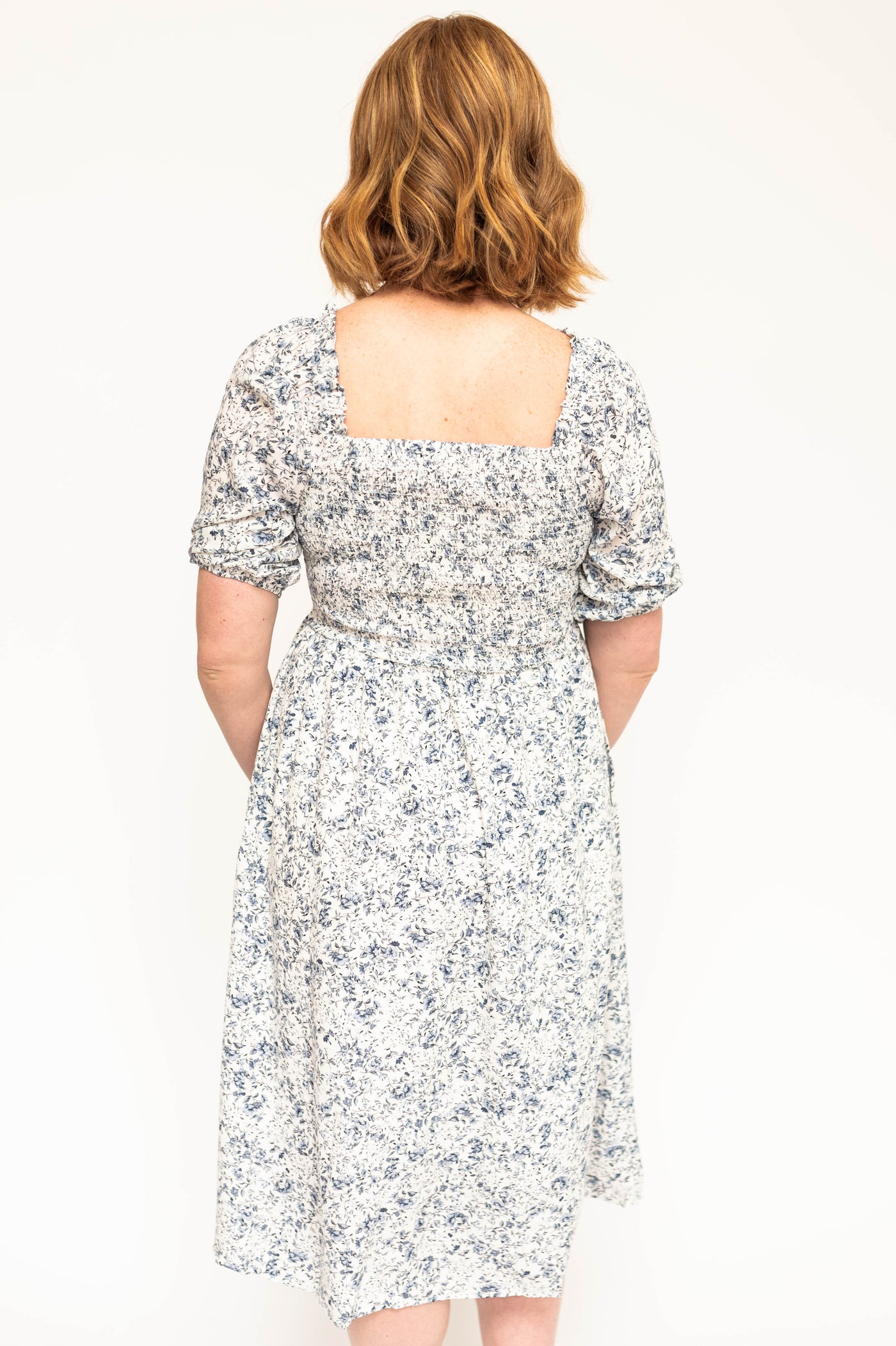 Back view of a blue and white short sleeve floral dress with a smocked bodice.