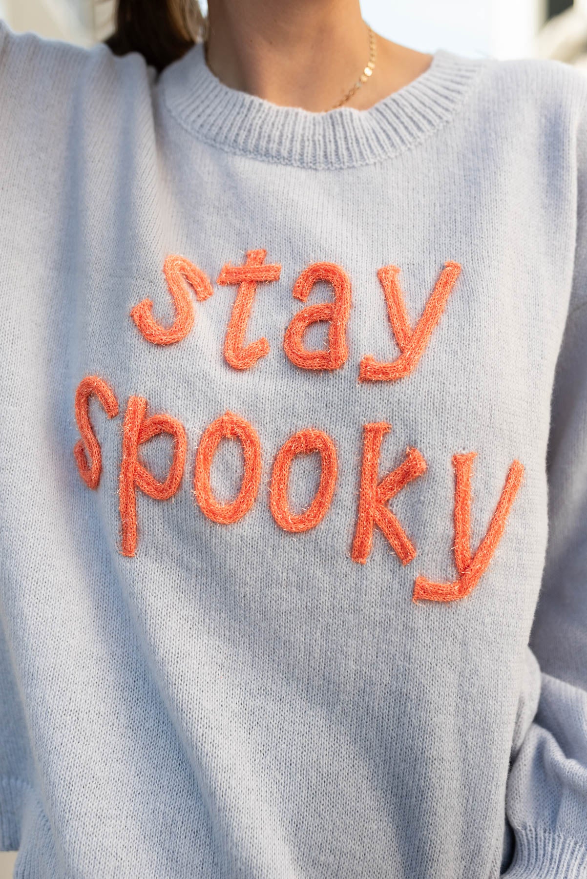 Close up of the stay spooky ligh grey sweater with orange lettering